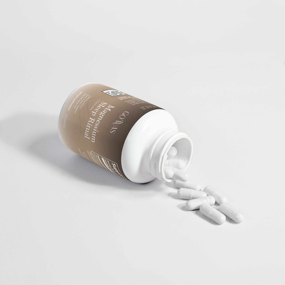 Magnesium Sleep Ritual supplement bottle with a taupe label and white capsules spilling from its open white container.